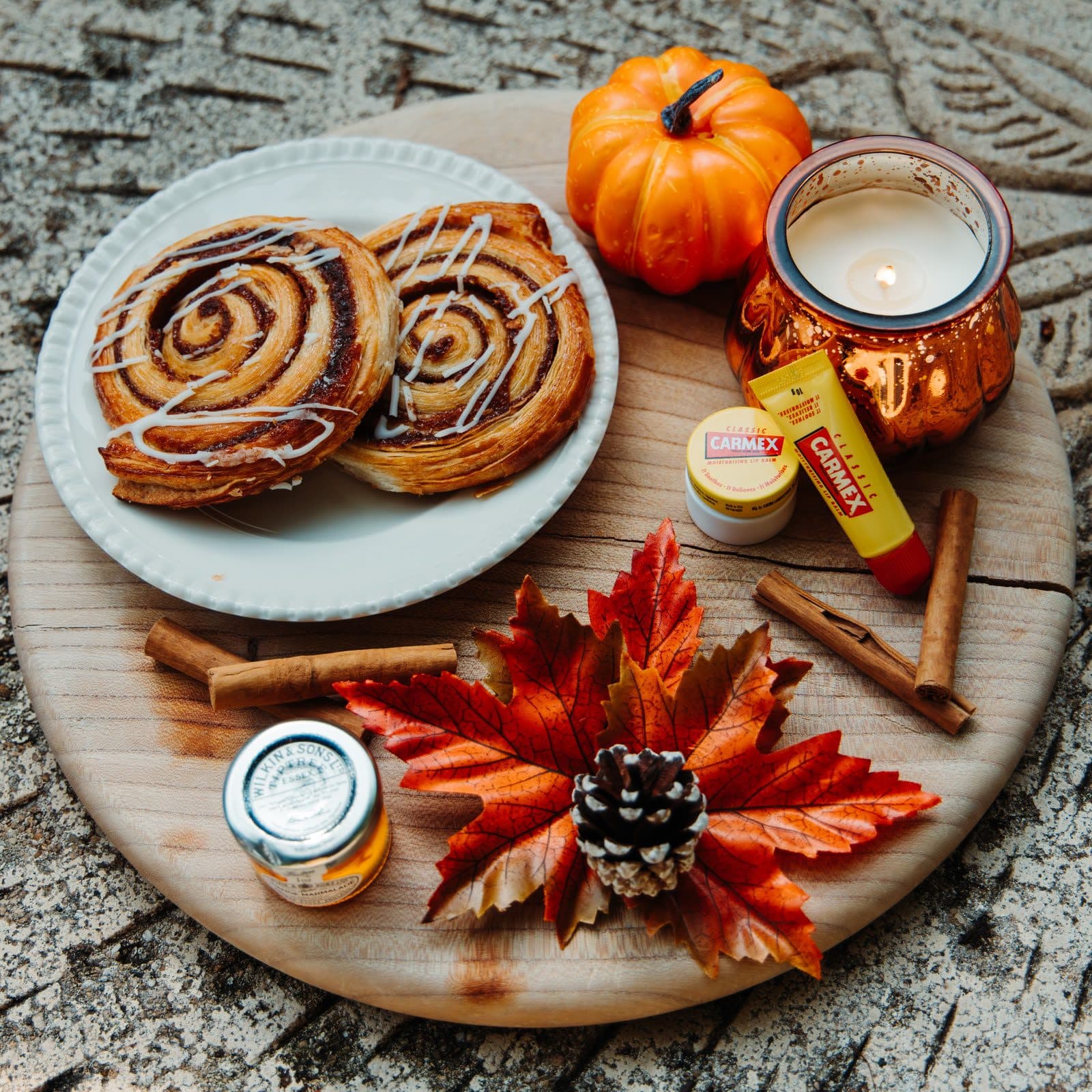 Tavola autunnale con girelle alla cannella, zucca e candela, con un vasetto e un tubetto Carmex